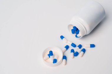 Blue-white pills spilling out of pill bottle on white background. Bottle of blue and white pills. Medicine. Medication
