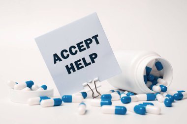 Text - Accept Help, written on sticky note near blue-white pills spilling out of pill bottle. Medical concept
