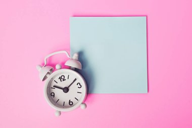 Boş yapışkan not ve pembe arkaplanda beyaz alarm saati, metin için kopyalama alanı olan şablon