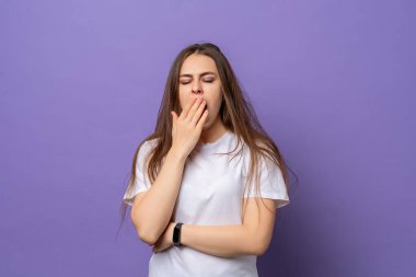 Uykucu kız, günlük tişört giyiyor. Ağzı eliyle kapatmaktan sıkılmış. Huzursuzluk ve uykusuzluk, mor arka planda tişört içinde durmak. Kronik yorgunluk sendromu, uykusuzluk ve enerji konsepti