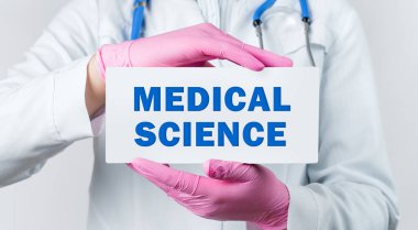 Beyaz önlüklü ve pembe steril eldivenli kadın doktorun elinde kelimelerin olduğu bir kart vardı. Tıp Bilimi. Tıbbi konsept