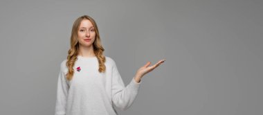 Mutlu sarışın genç bir kadının portresi, sağ elini göstererek tanıtım teklifinde, reklamda gri arka planda beyaz süveter giyiyor. Kopyalama alanı oluştur