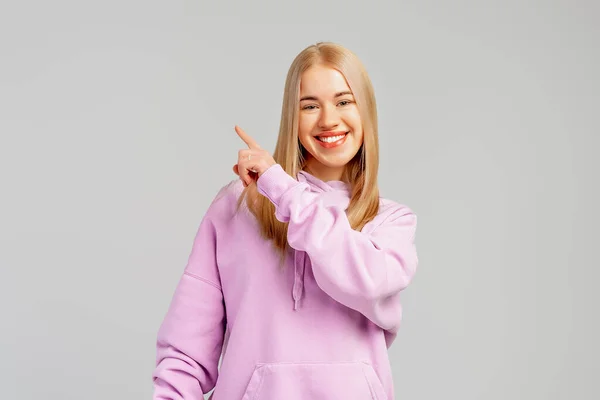 Lachend Stijlvol Blond Meisje Trendy Hoody Wijzende Vinger Links Tonen — Stockfoto