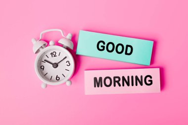 Pembe arka planda beyaz alarm saatinin yanında kağıda 