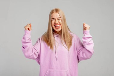 Mutlu sarışın kız başarı anının tadını çıkarıyor, zaferi ya da başarıyı kutluyor, neşeli hissediyor, önemli bir amaç ya da başarı kazanıyor, mor kapüşonlu giyinmiş evet hareketi yapıyor. Pozitif duygular