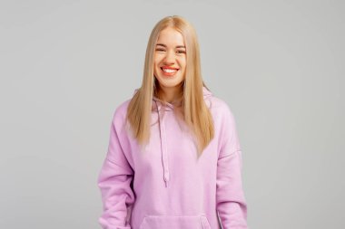 Genç sarışın bir kadının portresi, güzel bir gülümseme, stüdyoda gri arka planda poz veren güzel bir model.