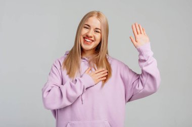 Mutlu sarışın genç kadın elini kaldırıyor ve kendini tanıtıyor, ben, kendi reklamını yapıyorum, gönüllü oluyorum, menekşe kabadayısı takıyorum, gri arka plana karşı duruyorum. Vücut dili kavramı