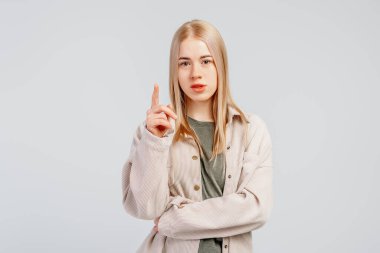 Kızgın, üzgün, sarışın kız, parmağıyla işaret eden ve hayal kırıklığına uğramış görünen, şikayet eden, adil olmayan bir şekilde somurtan, gri arka planda duran