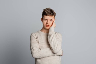 Günlük kıyafetler giyen, sıkılmış, yorgun ve dinlenmeye ihtiyacı olan, çalışma problemlerinden sıkılmış ve yorgun görünen, gri arka planda duran genç bir adam.