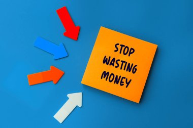 Parayı israf etmeyi bırak - yapışkan nota yazı konsepti. Turuncu kare yapışkan not ve mavi arkaplanda renkli oklar, üst görünüm