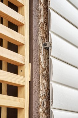 Bahar günü yakın görüşte modern beyaz plastik kaplamalarla kaplı kulübe duvarının yanında zarif ahşap ızgara ayırıcı