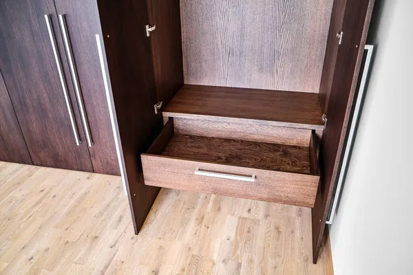 Open doors and drawer of elegant wardrobe made of dark oak veneer with shiny metal handles in minimal style in room closeup