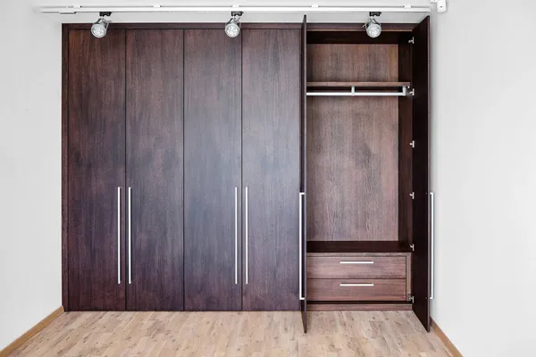 Open doors of elegant wardrobe with inner drawer made of dark oak veneer with shiny metal handles in minimal style in room