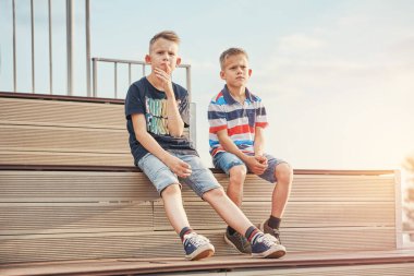 Okul çocukları şık giyinmiş arkadaşlar ahşap bankta oturup parktaki bulutlarla gökyüzüne karşı film izlerler.