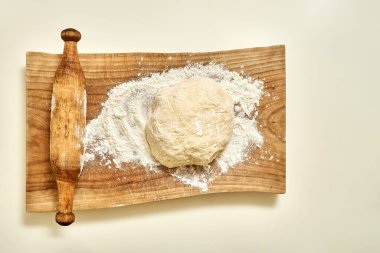 Tahta tahta kesme tahtası, hamur hamuruyla buğday unundan yapılan turtalar ve yukarıdan yakından görülen mutfak masasının üzerindeki eski tip yuvarlama iğne.