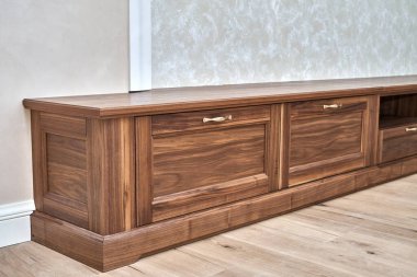 Zarif yeni televizyon dolabı, kaplama ve saf ceviz kerestesinden yapılmış. Duvarın yanında altın saplı, düşük açılı manzaralı.