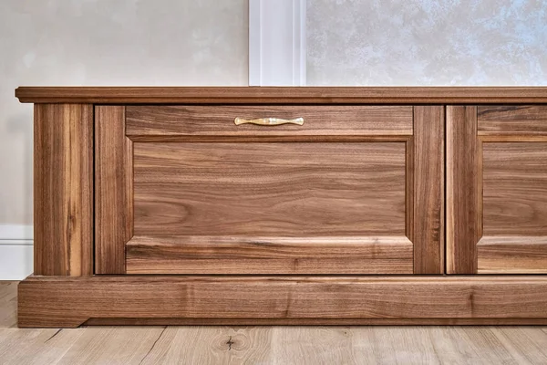 Elegant new TV cabinet made of veneer and solid walnut lumber with gold handles near wall in light room low angle view