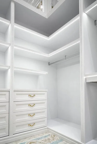 White corner wardrobe section with empty rack and led illumination on shelves in spacious walk-in closet in luxury apartment