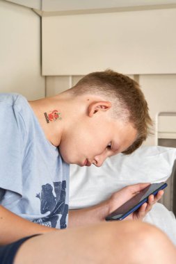 Kısa sarı saçlı genç, üst rafta oturan akıllı telefonlu elektronik kitap okuyor tren vagonunda yakın çekimde seyahat ediyor.