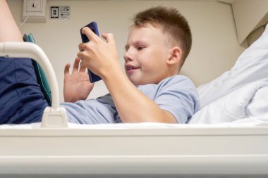 Kısa sarı saçlı genç, akıllı telefonlu elektronik kitapları okuyor. Beyaz yataklı vagonun üst rafında, düşük açılı çekimler yapıyor.