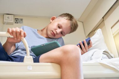 Ciddi sarışın liseli çocuk tablet bilgisayar ve telefonla oyun oynuyor. Aynı anda üst rafta oturuyor ve tren vagonunda yakın çekimde seyahat ediyor.