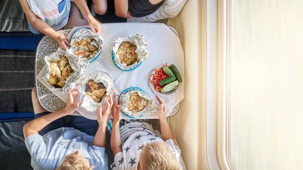 Mother and sons eat lunch at folded table traveling by train and sitting on bottom beds covered with blankets close upper view