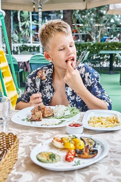 Ragazzo Morde Mastica Pezzo Carne Sulla Forchetta Mangiare Tavolo All Foto Stock