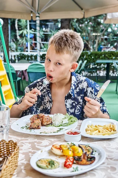 Ragazzo Morde Mastica Pezzo Carne Sulla Forchetta Mangiare Tavolo All Foto Stock