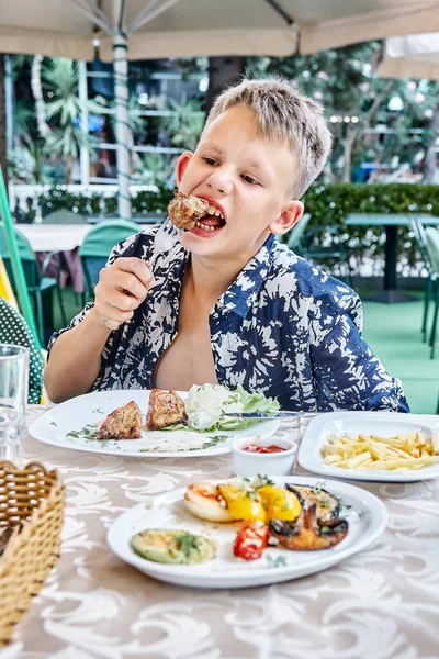 Ragazzo Morde Mastica Pezzo Carne Sulla Forchetta Mangiare Tavolo All Immagine Stock