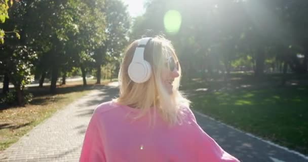 Junge Frau mit Kopfhörern tanzt fröhlich auf Parkbank — Stockvideo
