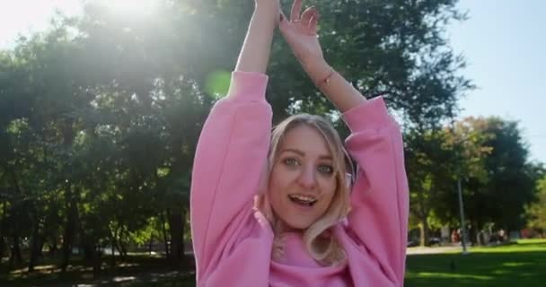 Blondynka młoda kobieta w słuchawkach tańczy i pozuje w parku — Wideo stockowe