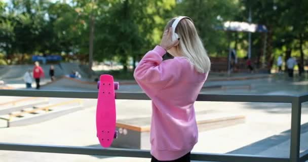 Senhora caminha com penny board ouvindo música em fones de ouvido — Vídeo de Stock