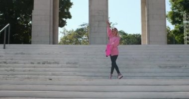 Genç bir kadın elinde bozuk parayla parkın merdivenlerinde dans ediyor.