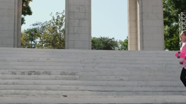 Mladá žena dělá split na schodišti v parku drží penny palubě — Stock video