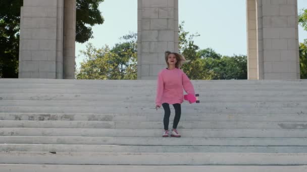 Jovem mulher salta e sorri alegremente segurando penny board — Vídeo de Stock