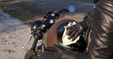 Sarışın kadın motosikletçi kask siperliğini kumaşla temizliyor.
