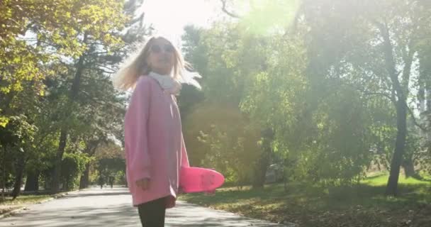 ヘッドフォンを持つ女性は公園の路地を歩き、ポーズを変える — ストック動画