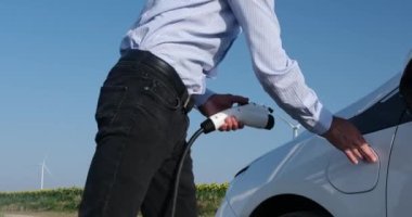 Yel değirmenleri, şarj aletini elektrikli arabaya bağlayan adamın arkasında döner.