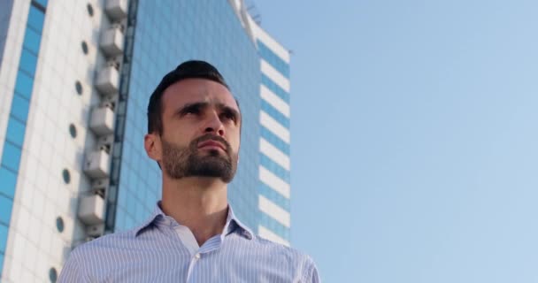 Человек надевает шлем, стоя напротив высотного офисного здания — стоковое видео