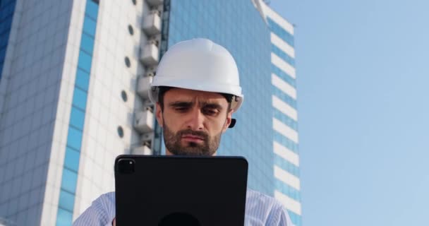 Ingeniero trabaja a través de tableta de pie contra edificio de gran altura — Vídeos de Stock