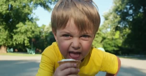 Biondo ragazzo lecca gelato in cialda cono in piedi su strada — Video Stock