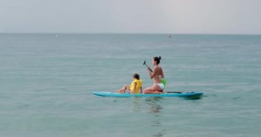 Kadın ve kız sakin denizde kürek çekiyor.