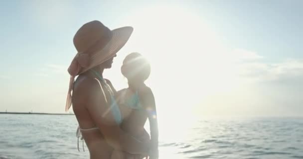 Woman holds and hugs girl standing on beach at sunlight — Vídeo de Stock