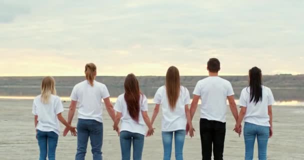 Team of friends raises hands holding together on river bank — Stock Video