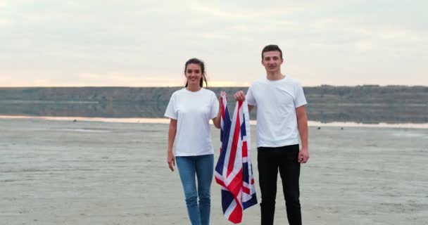 Couple unfolds showing British flag on flat river bank — стокове відео