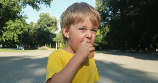 Child in t-shirt eats ice cream in waffle cone on street — Stockvideo