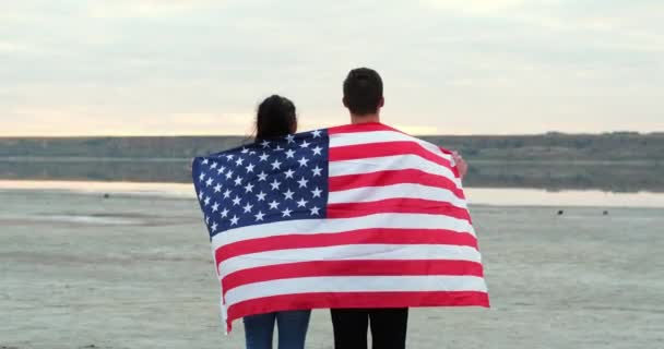 Couple stands covered with American flag against calm river — Video Stock