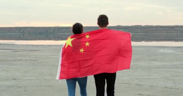 Young man and woman lift Chinese flag walking on river bank — стокове відео