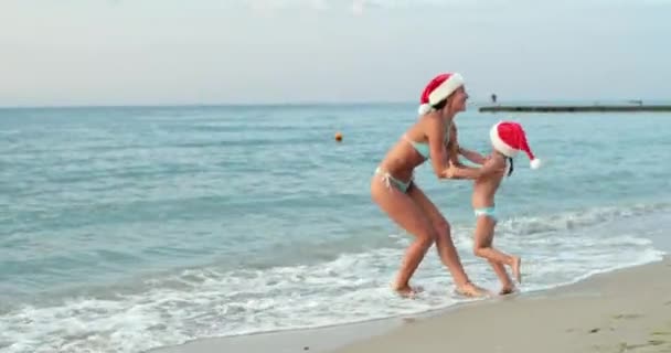 Woman and girl spin relaxing on beach by sea in Santa hats — стокове відео