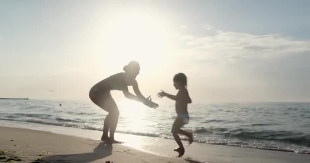 Mother catches girl in arms resting on sea beach at sunlight — 图库视频影像